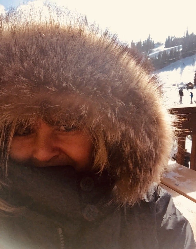 Diana Kramer, Life Enrichment Coordinator, bundled in a fur-hooded jacket on a snowy, sunny day outdoors.