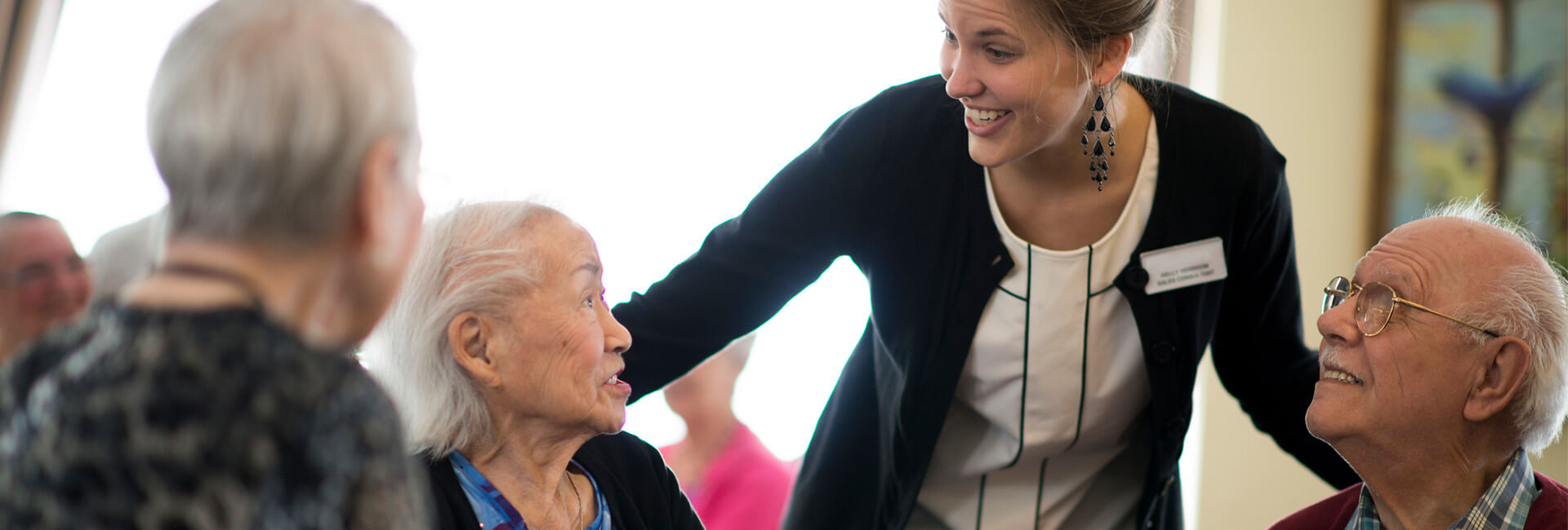 Staff member engaging with senior residents in a dining area.