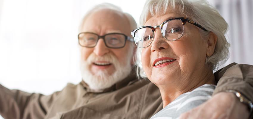 Elderly couple smiling and sitting together in a cozy living space.