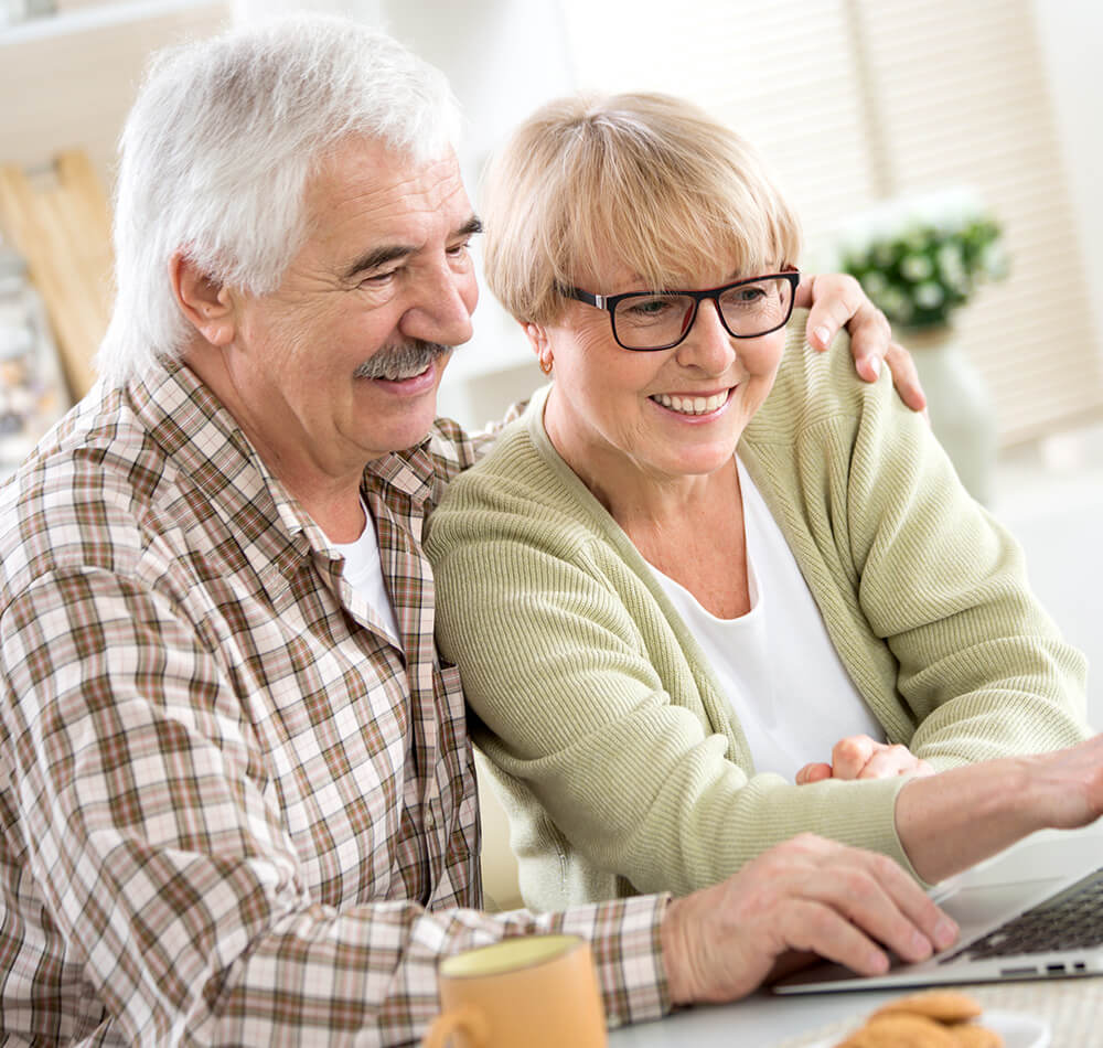 Smiling senior couple using a laptop in a bright, cozy room.