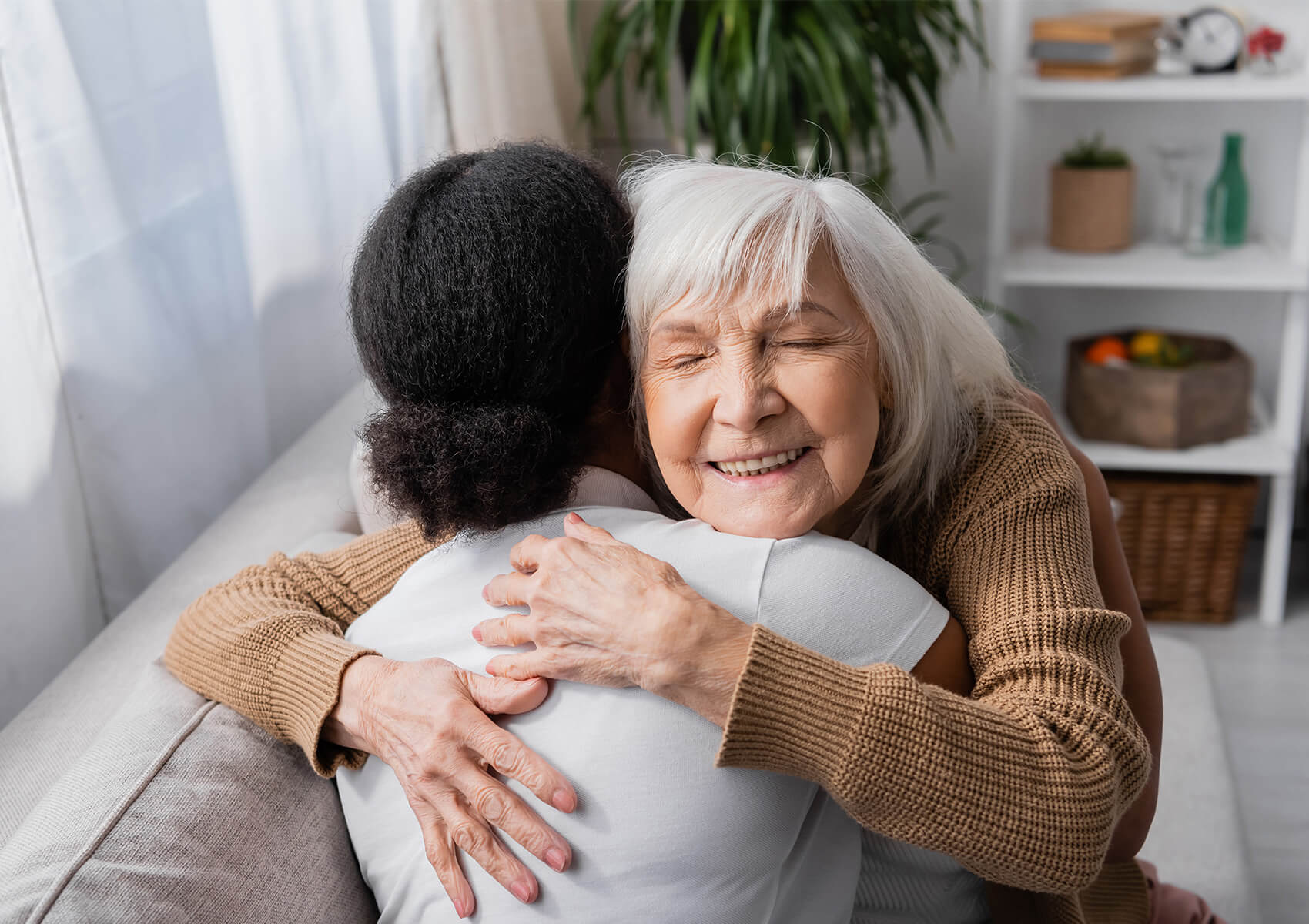Elderly woman embracing a young caregiver in a cozy living room setting.