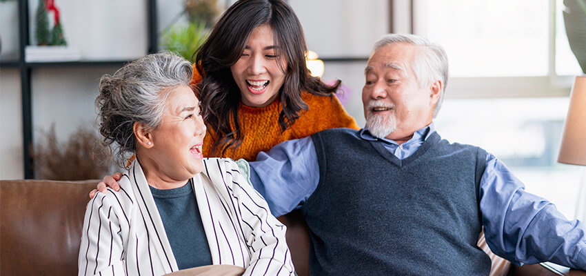 Two seniors and a young woman laughing together on a living room sofa.