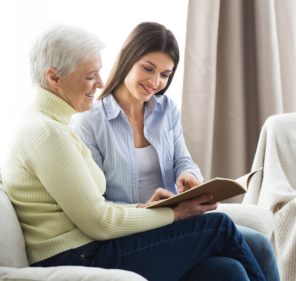 Young woman reading a book with an elderly woman on a cozy sofa.