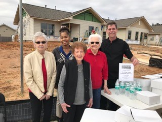 Group of five people in front of partially constructed residential units holding refreshments.