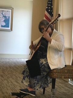 Person playing guitar while seated indoors near an American flag and a floral painting.