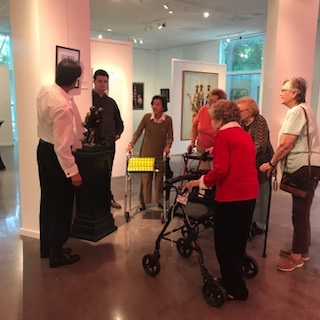 A group of seniors viewing statues and artwork in a gallery with a guide explaining the pieces.