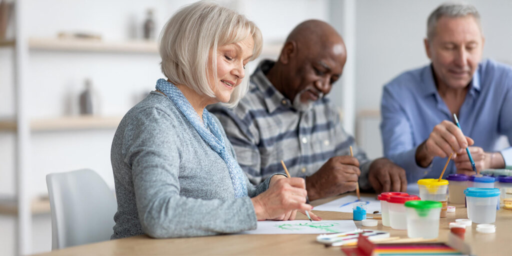 Woman smiles as she and two men paint pictures at a table